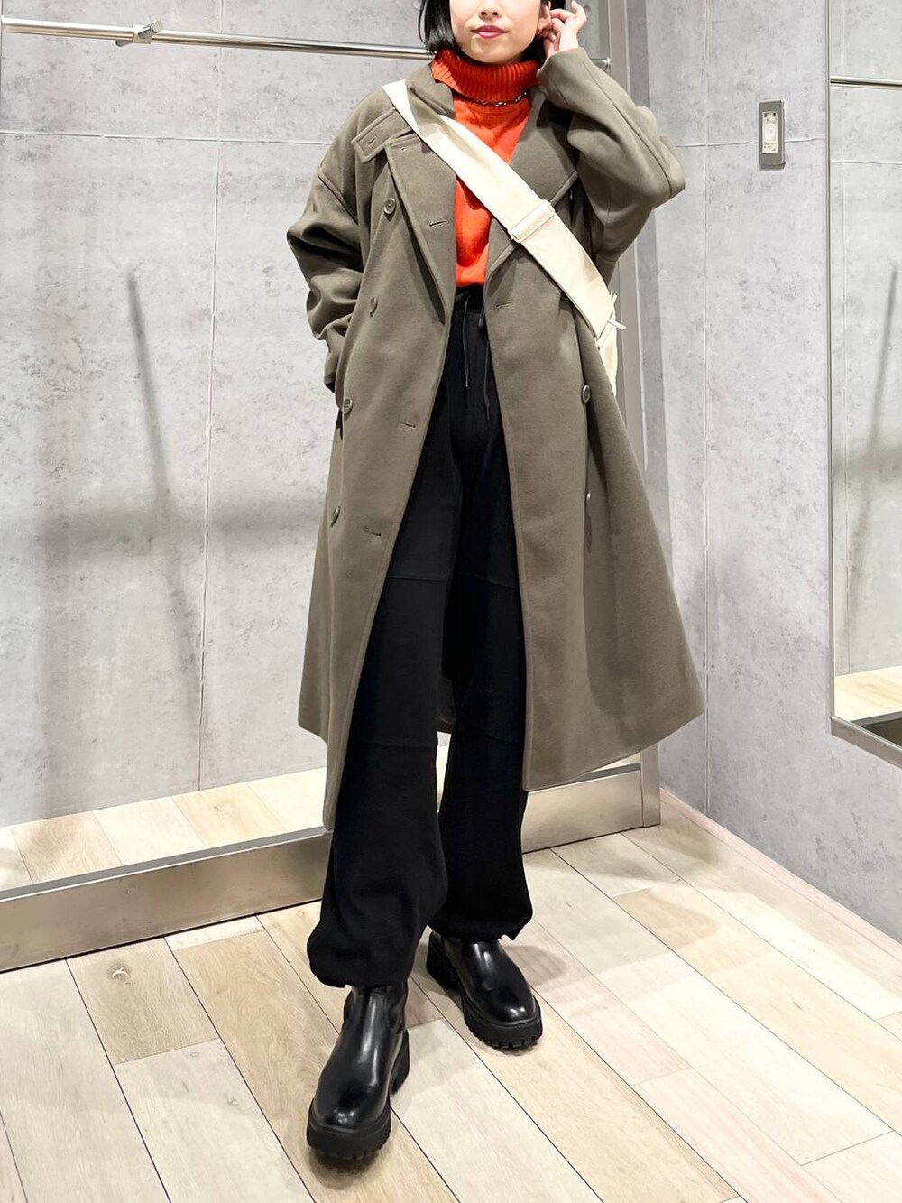 レッド系のニット/セーター、グリーン系のチェスターコート、ブラック系のブーツを着用したレディースの冬コーディネートの6枚目の写真