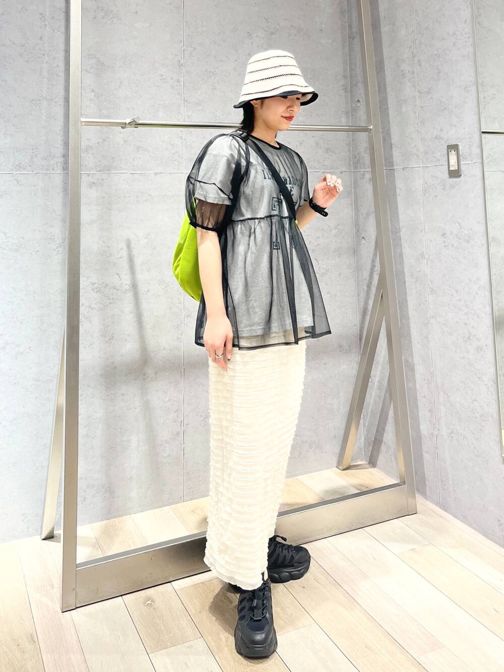 ブラック系のスニーカー、ホワイト系のスカート、グリーン系のショルダーバッグを着用したレディースの春コーディネートの2枚目の写真