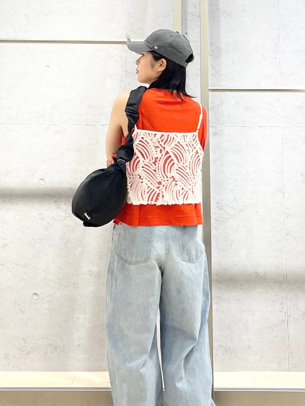 オレンジ系のタンクトップ、ブラック系のショルダーバッグ、ブルー系のデニムパンツを着用したレディースの夏コーディネートの3枚目の写真