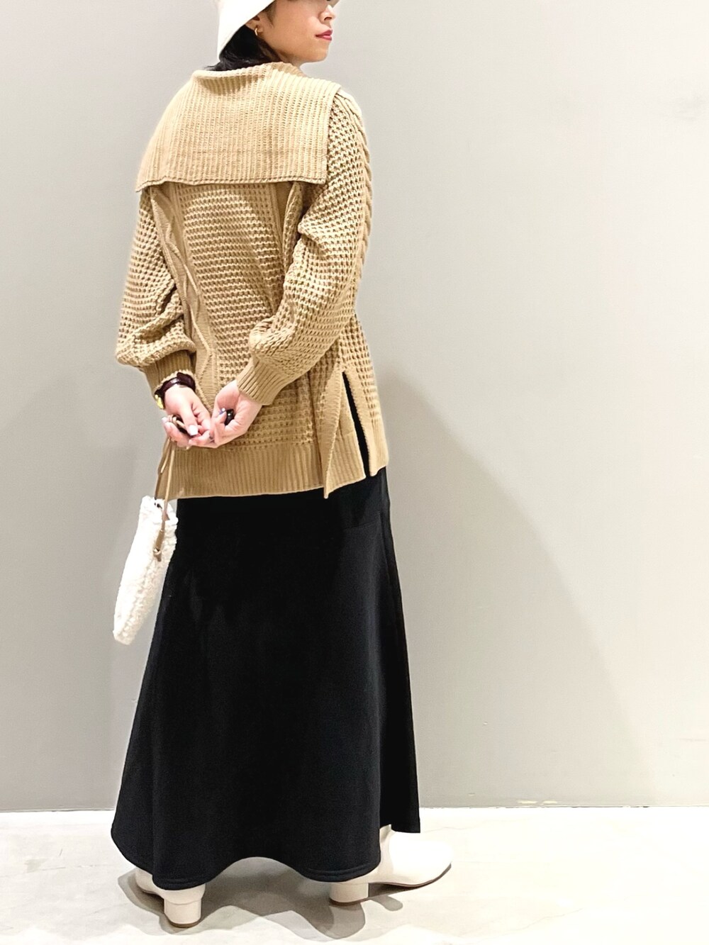 イエロー系のニット/セーター、ブラック系のスカート、ホワイト系のブーツを着用したレディースの秋コーディネートの4枚目の写真