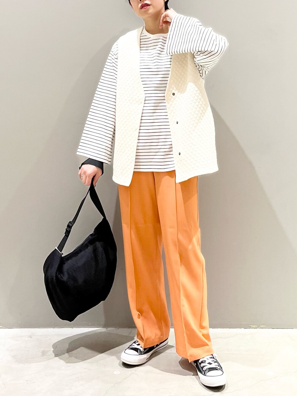 ブラック系のスニーカー、オレンジ系のスラックス、ホワイト系のトップスを着用したレディースの春コーディネートの4枚目の写真