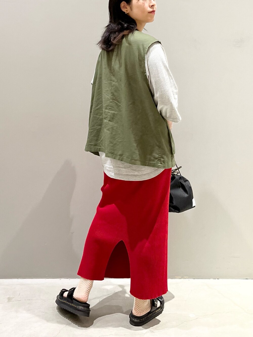 レッド系のスカート、ブラック系のサンダル、ブラック系のショルダーバッグを着用したレディースの秋コーディネートの2枚目の写真