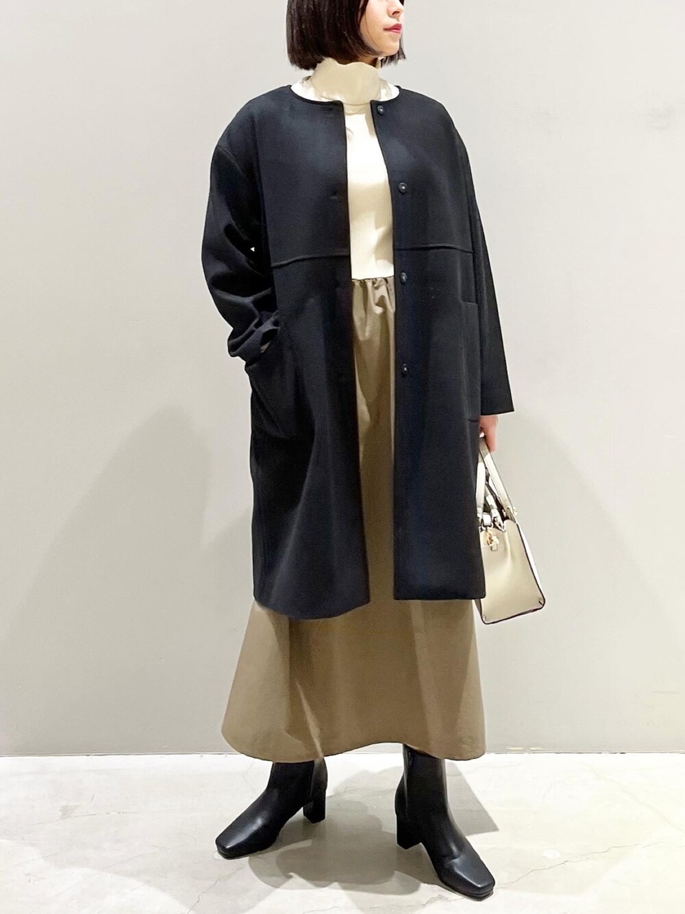 ブラック系のジャケット/アウター、グリーン系のワンピース、ホワイト系のショルダーバッグを着用したレディースの冬コーディネートの2枚目の写真