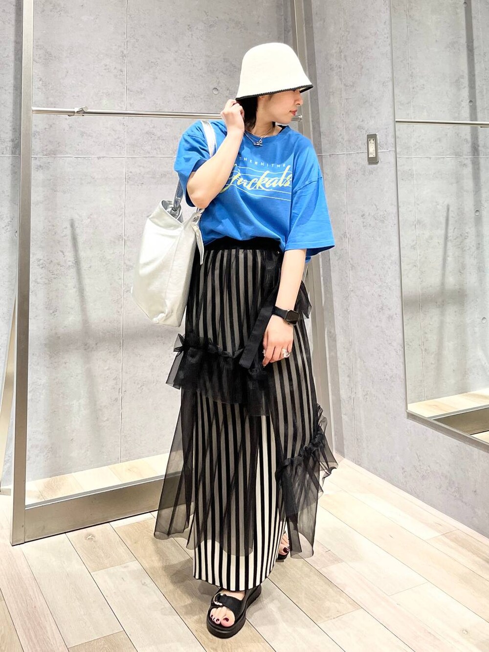 ホワイト系のスカート、ブルー系のTシャツ/カットソー、ブラック系のサンダルを着用したレディースの春コーディネートの3枚目の写真