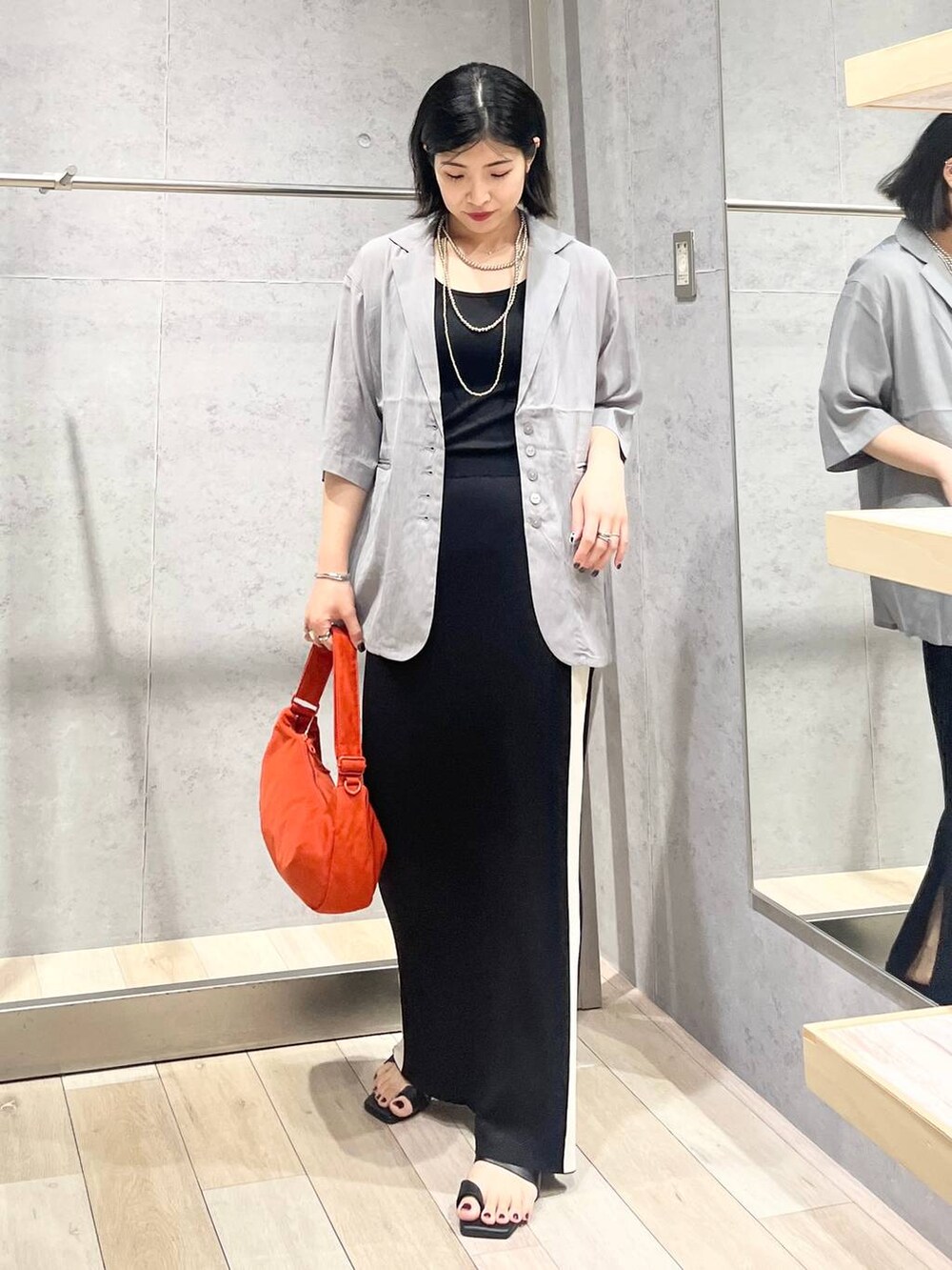 ブラック系のスカート、ブラック系のサンダル、オレンジ系のショルダーバッグを着用したレディースの夏コーディネートの5枚目の写真