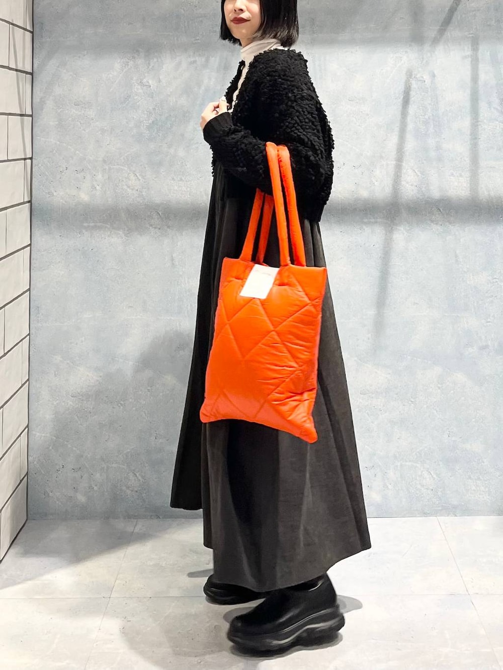 オレンジ系のトートバッグ、グレー系のワンピース、ブラック系のブーツを着用したレディースの冬コーディネートの4枚目の写真