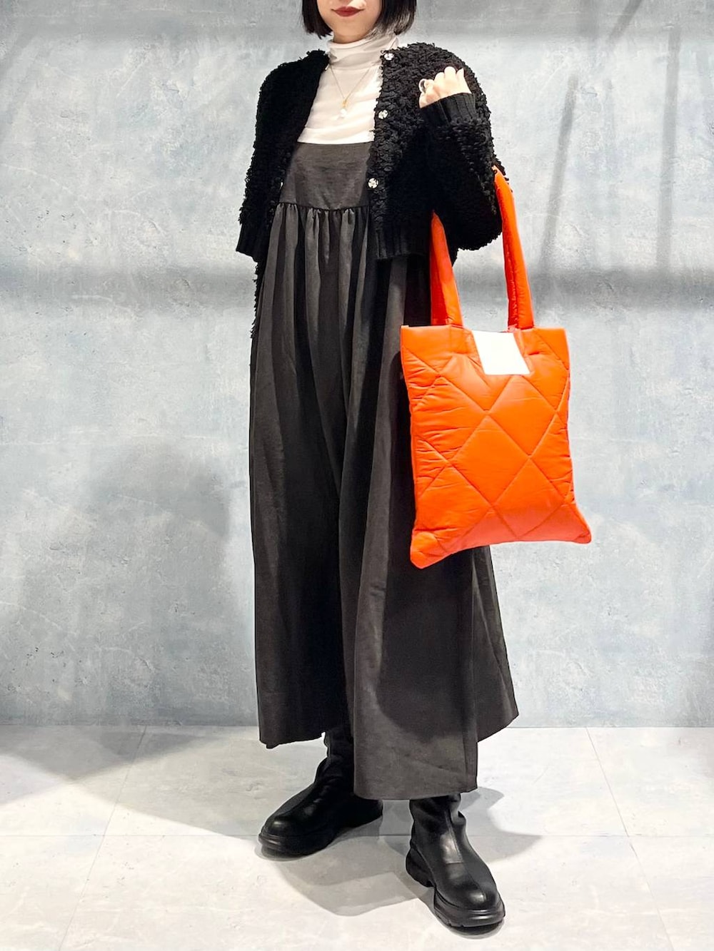 オレンジ系のトートバッグ、グレー系のワンピース、ブラック系のブーツを着用したレディースの冬コーディネートの7枚目の写真
