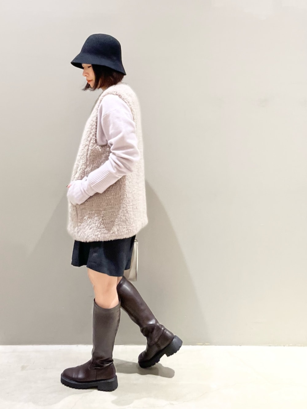 ブラウン系のブーツ、ホワイト系のショルダーバッグ、ブラック系のパンツを着用したレディースの冬コーディネートの2枚目の写真