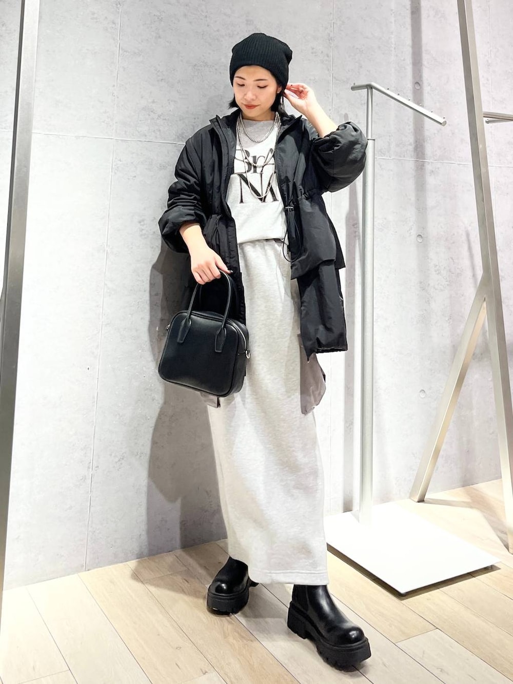 グレー系のスカート、ブラック系のボストンバッグ、ブラック系のブーツを着用したレディースの秋コーディネートの2枚目の写真