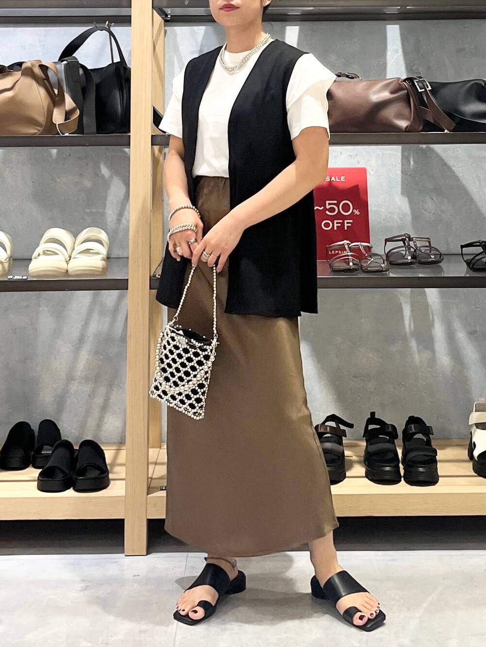 シルバー系のショルダーバッグ、ブラウン系のスカート、ブラック系のサンダルを着用したレディースの夏コーディネートの2枚目の写真