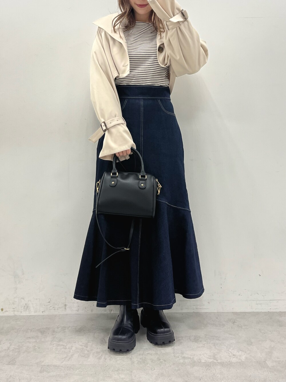 ベージュ系のトレンチコート、ブラック系のTシャツ/カットソー、ブルー系のスカートを着用したレディースの冬コーディネートの3枚目の写真