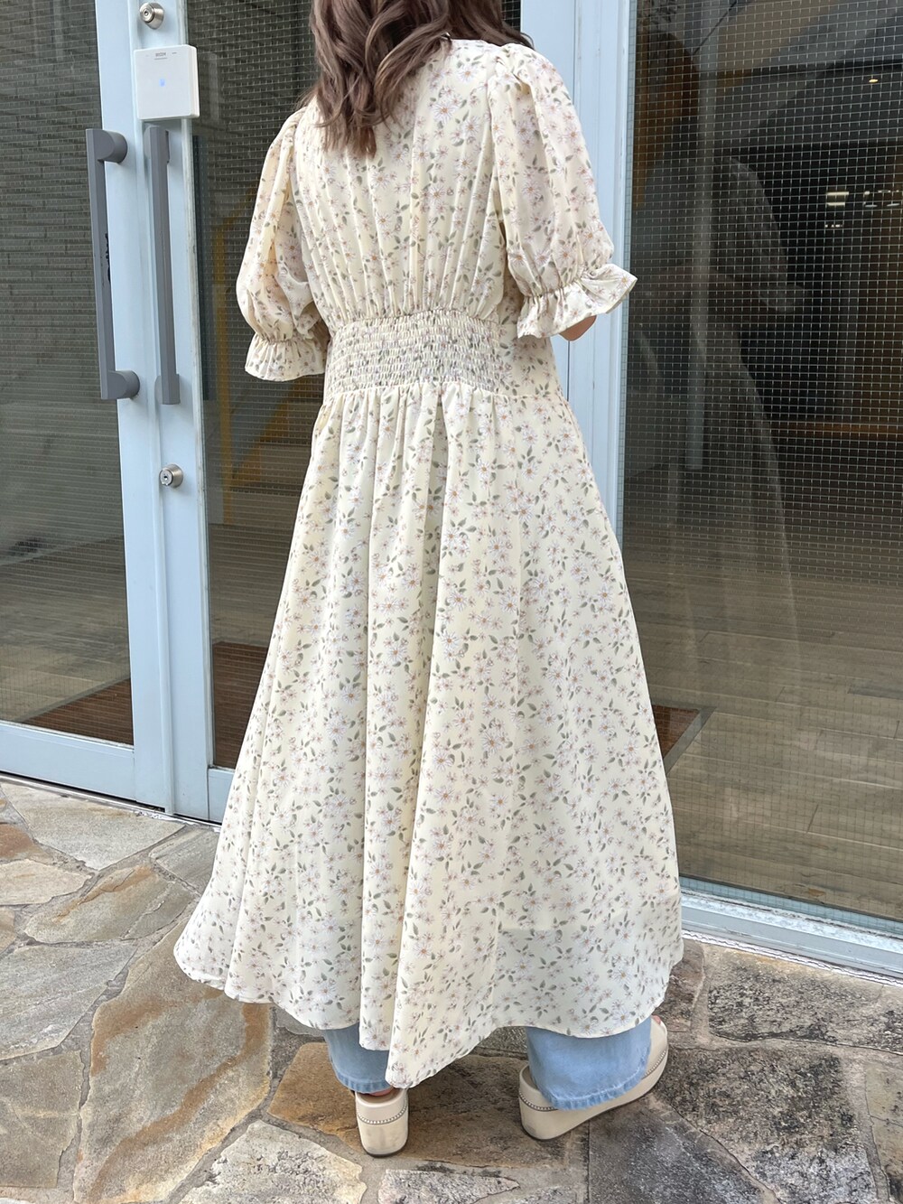 イエロー系のワンピース、ブルー系のデニムパンツ、ホワイト系のショルダーバッグを着用したレディースの春コーディネートの2枚目の写真