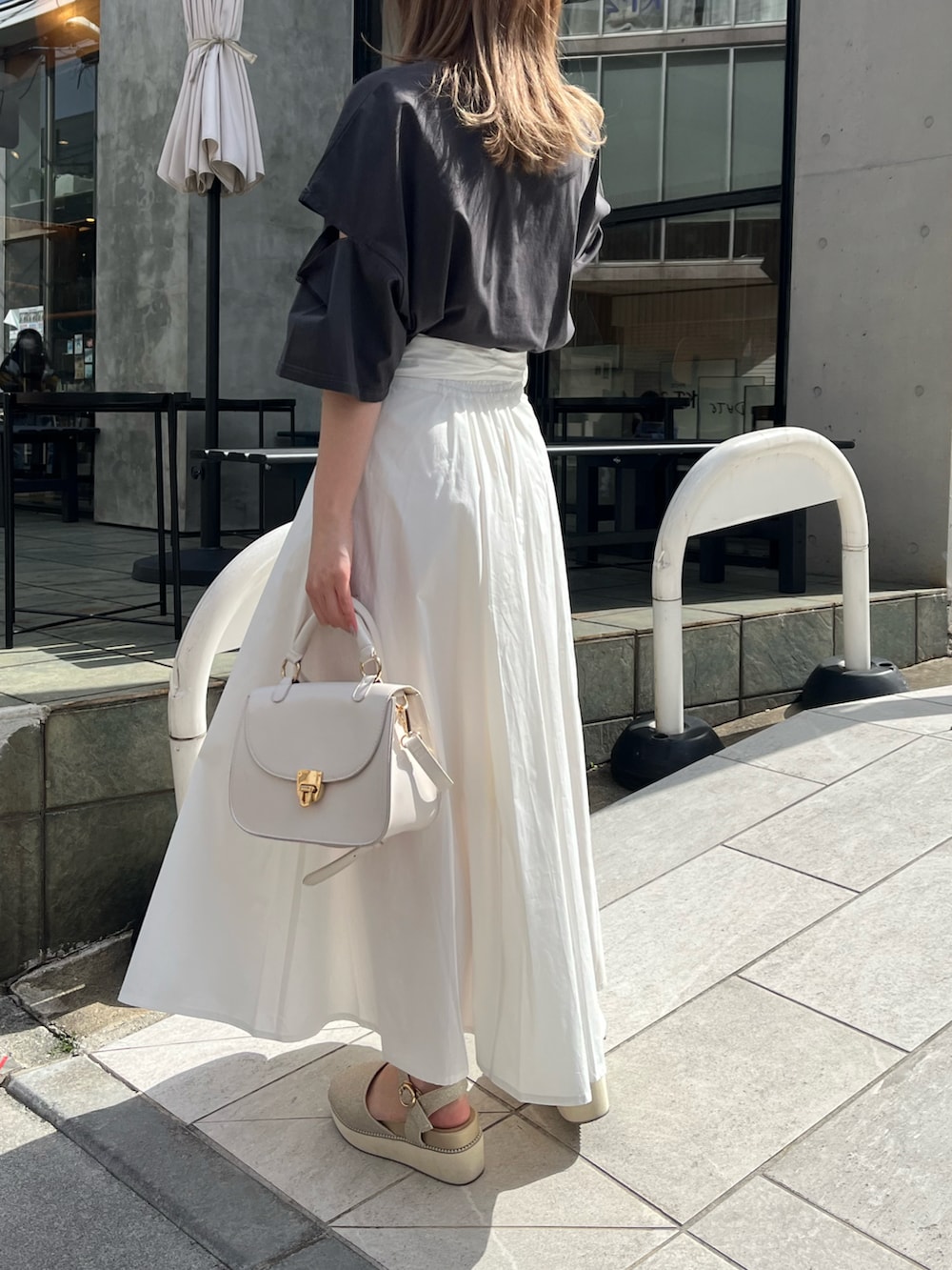 ブラック系のTシャツ/カットソー、ホワイト系のスカート、ゴールド系のサンダルを着用したレディースの春コーディネートの2枚目の写真