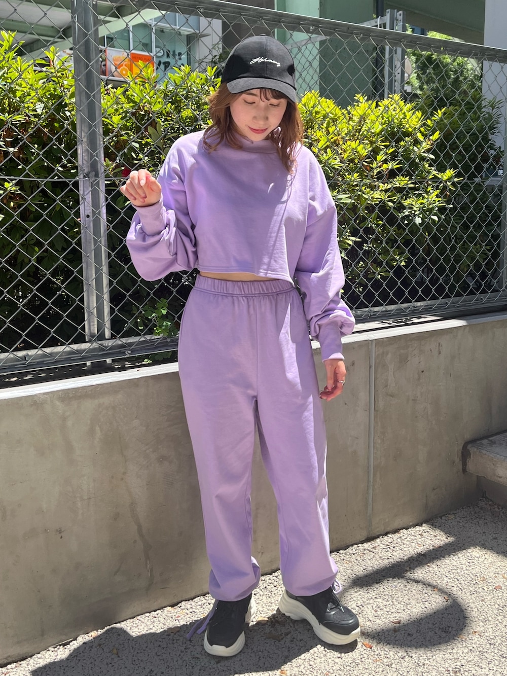 パープル系のスウェット、パープル系のスウェットパンツ、ブラック系のスニーカーを着用したレディースの夏コーディネートの2枚目の写真