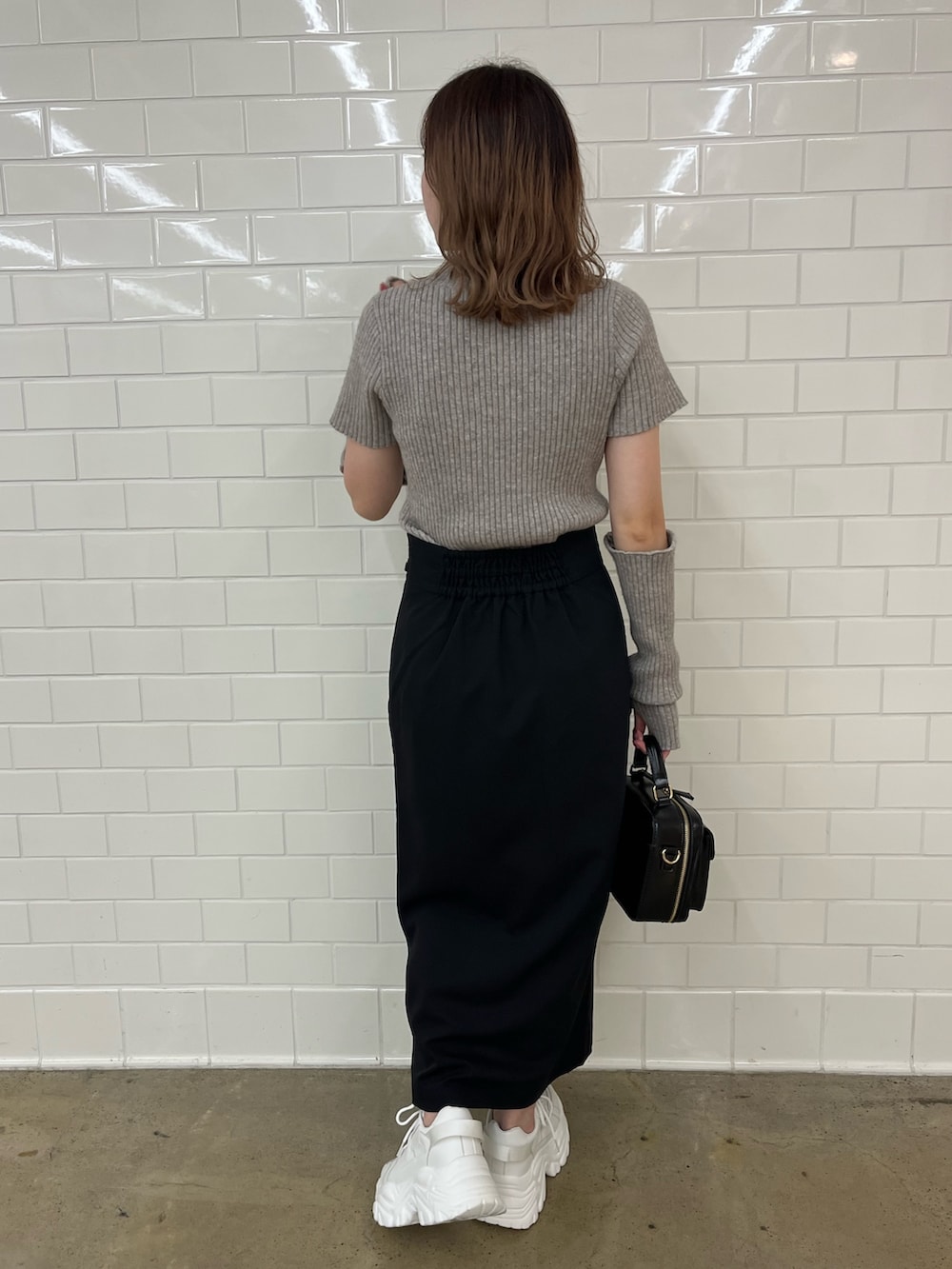 ブラウン系のニット/セーター、ブラック系のスカート、ホワイト系のスニーカーを着用したレディースの夏コーディネートの2枚目の写真