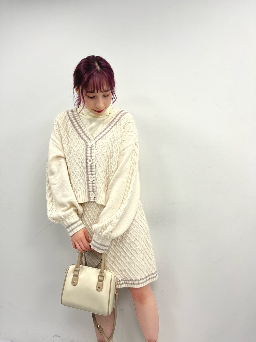 パープル系のワンピース、ホワイト系のニット/セーター、ホワイト系のブーツを着用したレディースの冬コーディネートの2枚目の写真