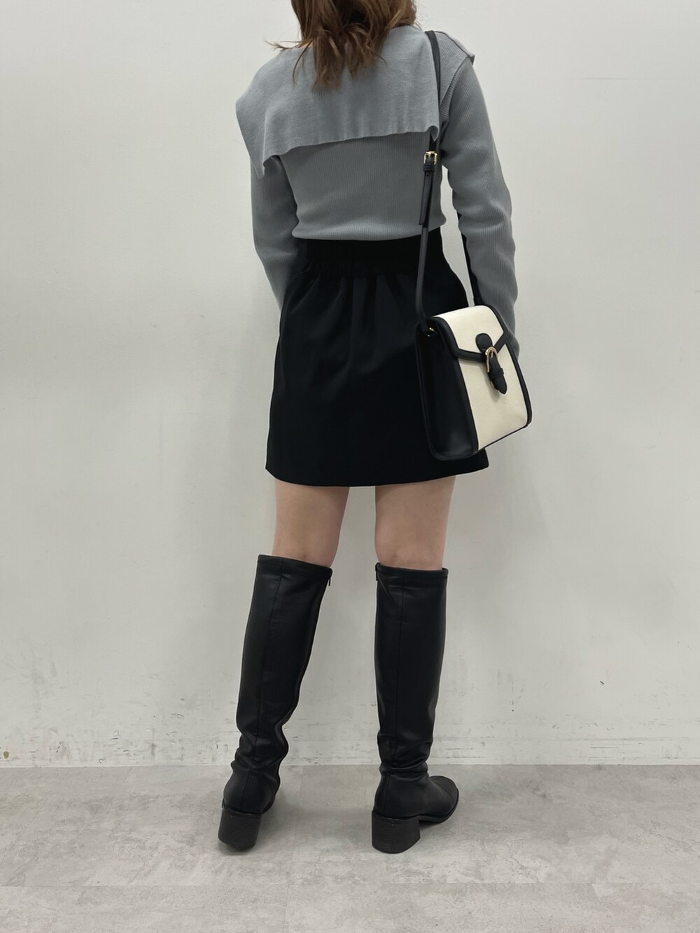 グレー系のニット/セーター、ブラック系のスカート、ブラック系のブーツを着用したレディースの冬コーディネートの2枚目の写真