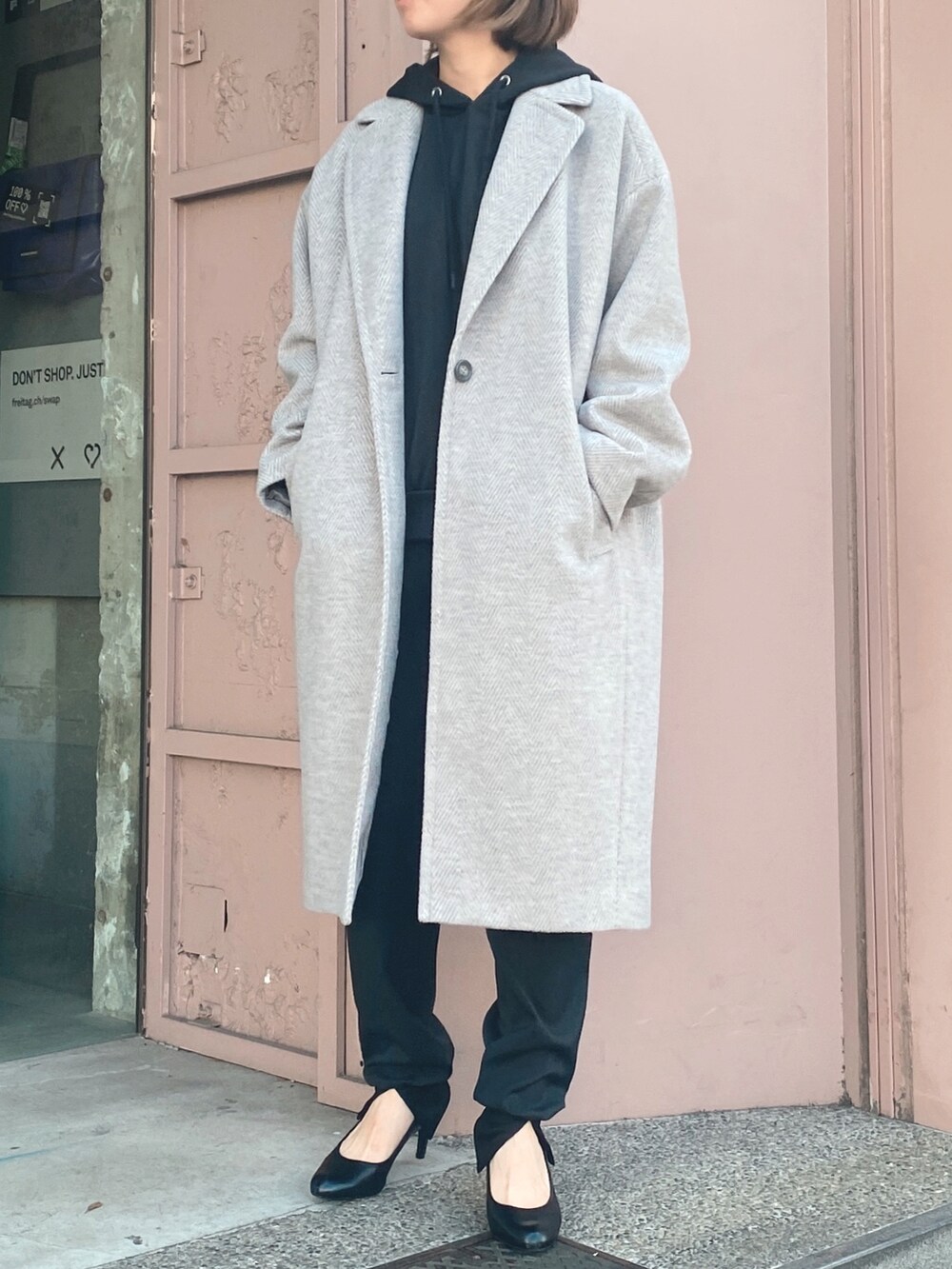 グレー系のチェスターコート、ブラック系のその他パンツ、ブラック系のパーカーを着用したレディースの冬コーディネートの2枚目の写真