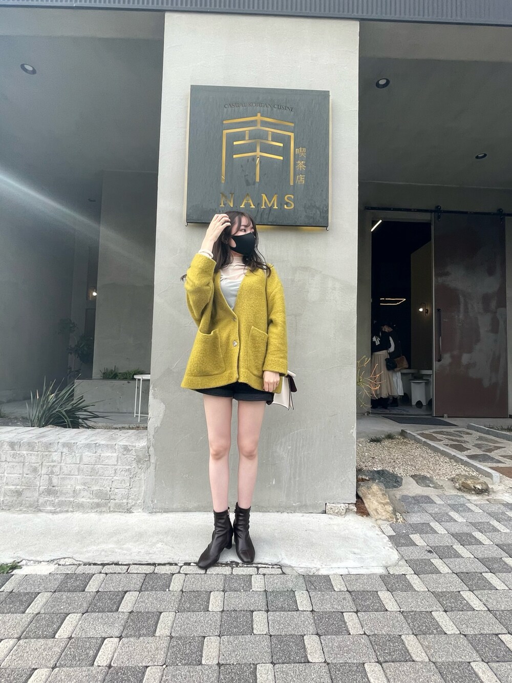 イエロー系のニット/セーター、ブラウン系のブーツ、ブラック系のデニムパンツを着用したレディースの冬コーディネートの2枚目の写真