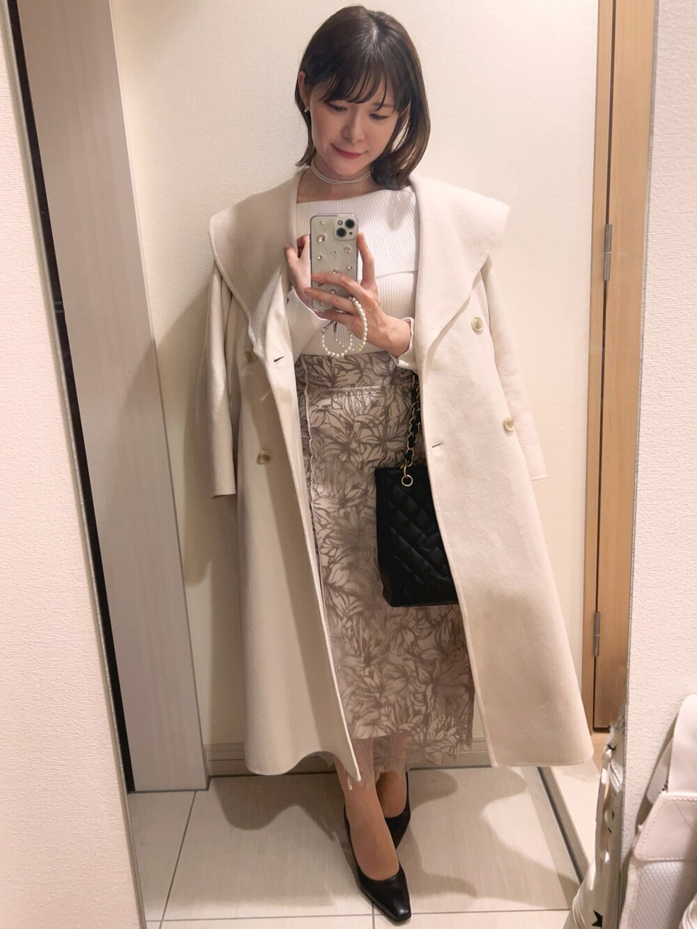 ブラック系のハンドバッグ、ホワイト系のニット/セーター、ベージュ系のスカートを着用したレディースの春コーディネートの2枚目の写真