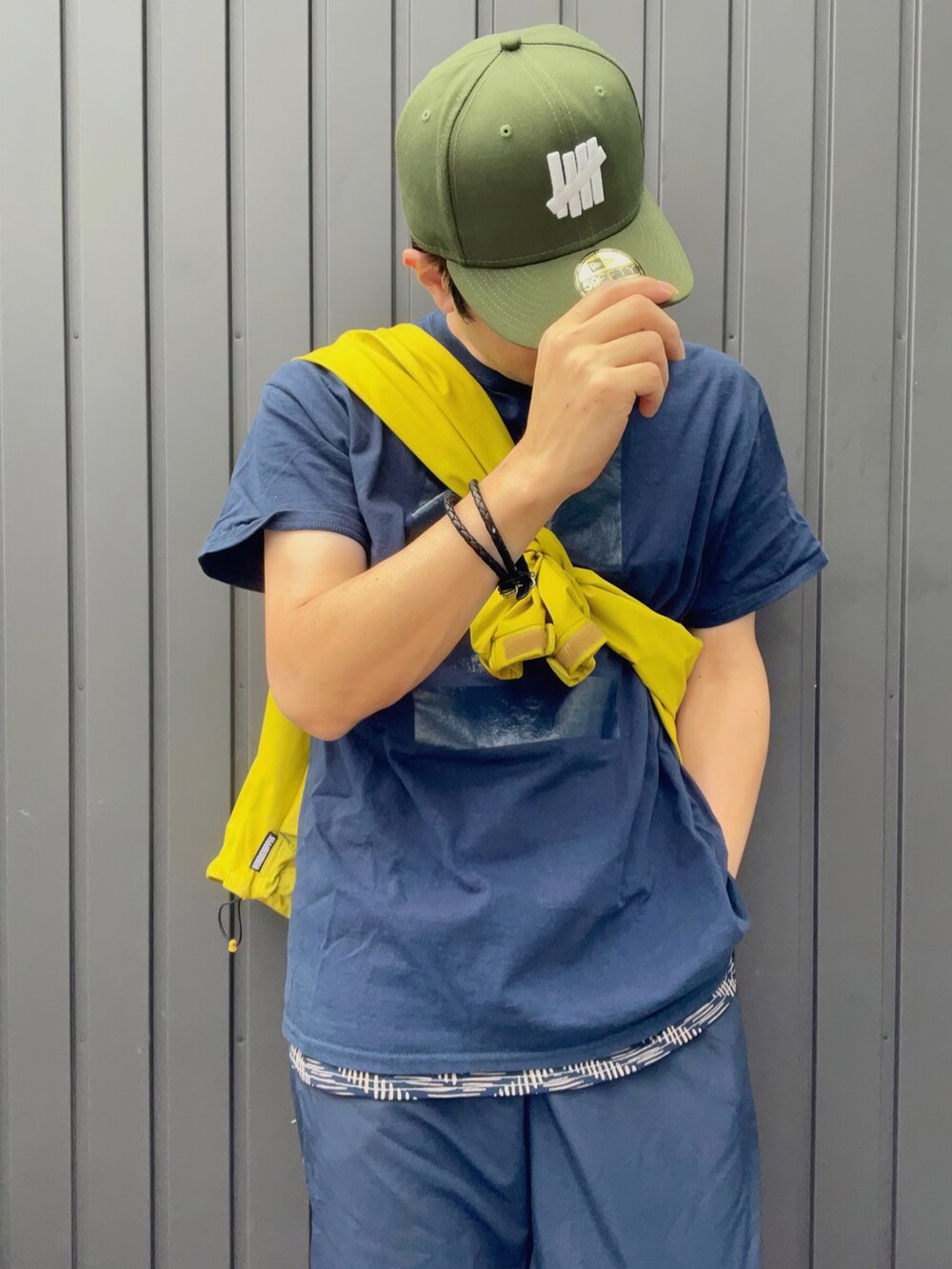 イエロー系のナイロンジャケット、ブルー系のTシャツ/カットソー、ベージュ系のタンクトップを着用したメンズの夏コーディネートの2枚目の写真