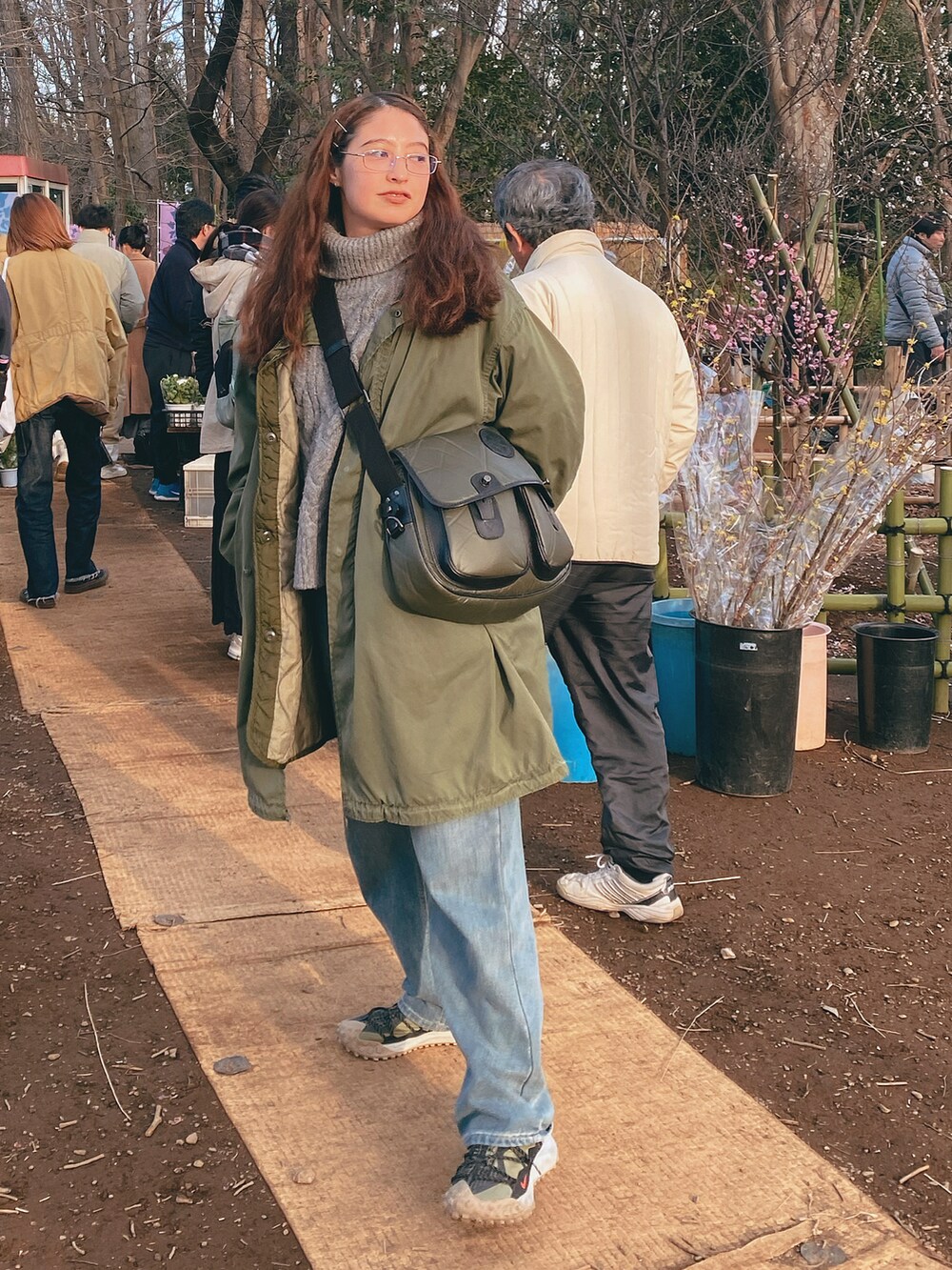 ブルー系のデニムパンツ、ブラウン系のスニーカー、グリーン系のショルダーバッグを着用したレディースの冬コーディネートの4枚目の写真