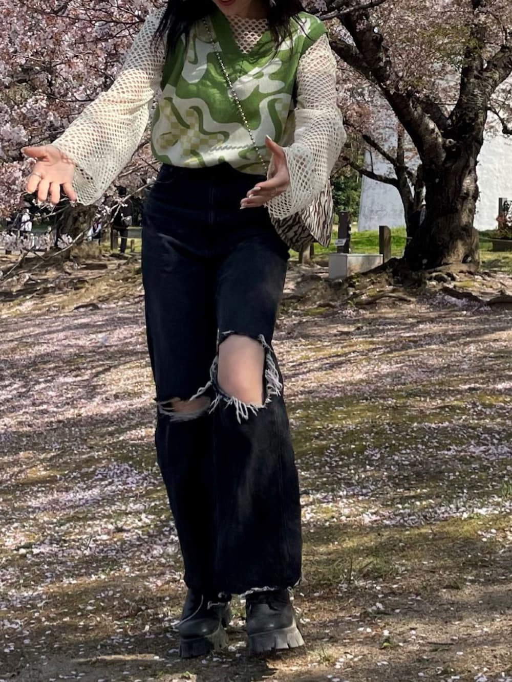 ブラック系のデニムパンツ、ブラック系のブーツ、グリーン系のベストを着用したレディースの春コーディネートの3枚目の写真