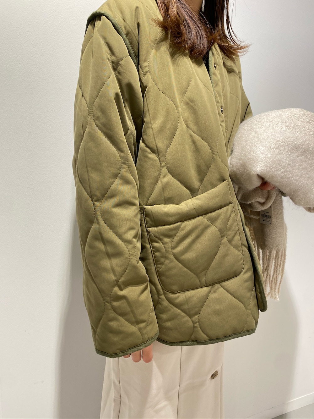 グリーン系のナイロンジャケット、ホワイト系のジャンパースカート、ブラック系のブーツを着用したレディースの秋コーディネートの3枚目の写真