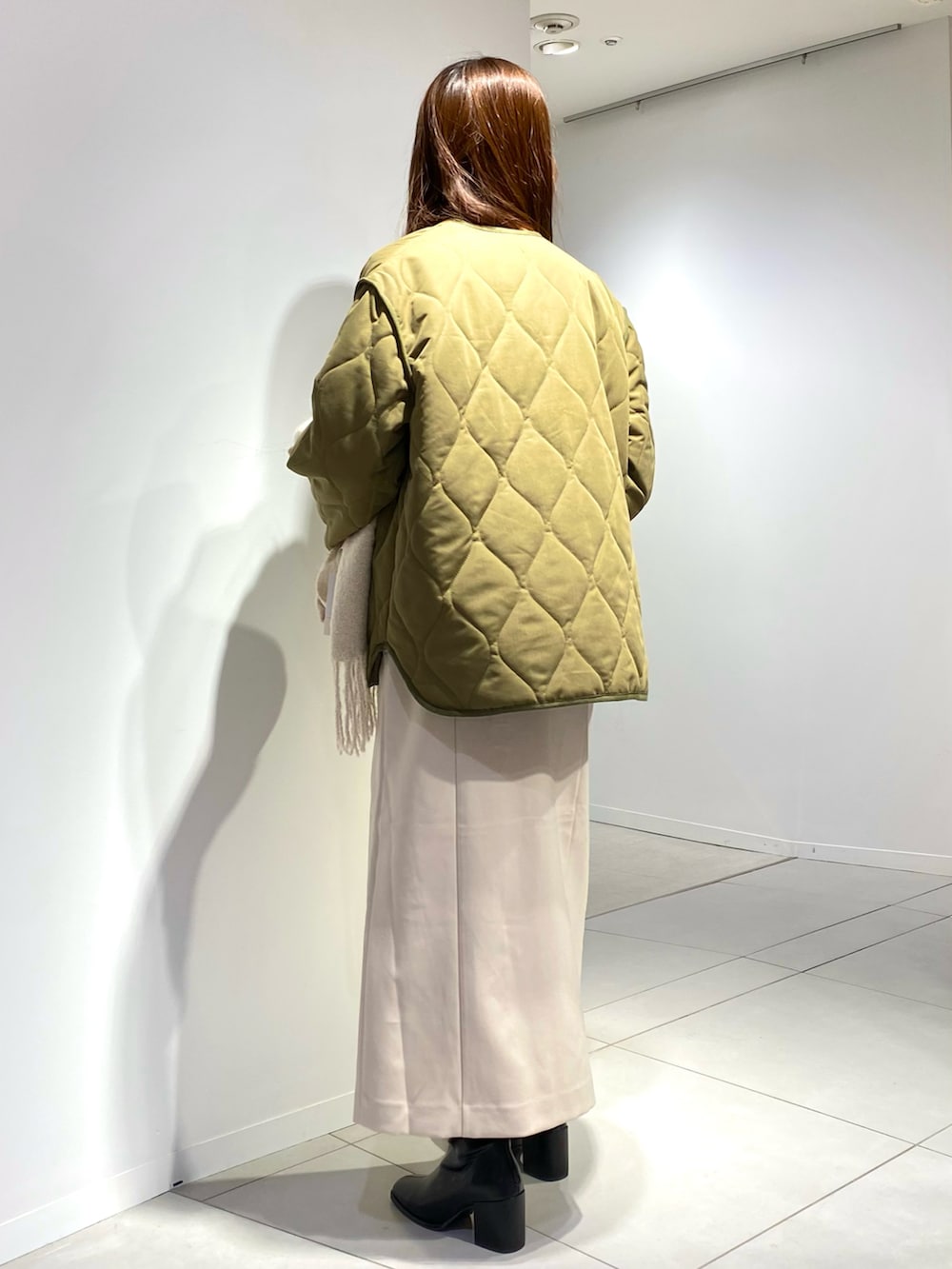 グリーン系のナイロンジャケット、ホワイト系のジャンパースカート、ブラック系のブーツを着用したレディースの秋コーディネートの2枚目の写真