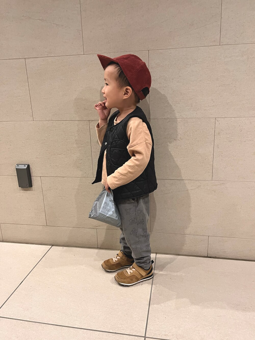オレンジ系のTシャツ/カットソー、ブラック系のダウンベスト、グレー系のパンツを着用したキッズの秋コーディネートの2枚目の写真