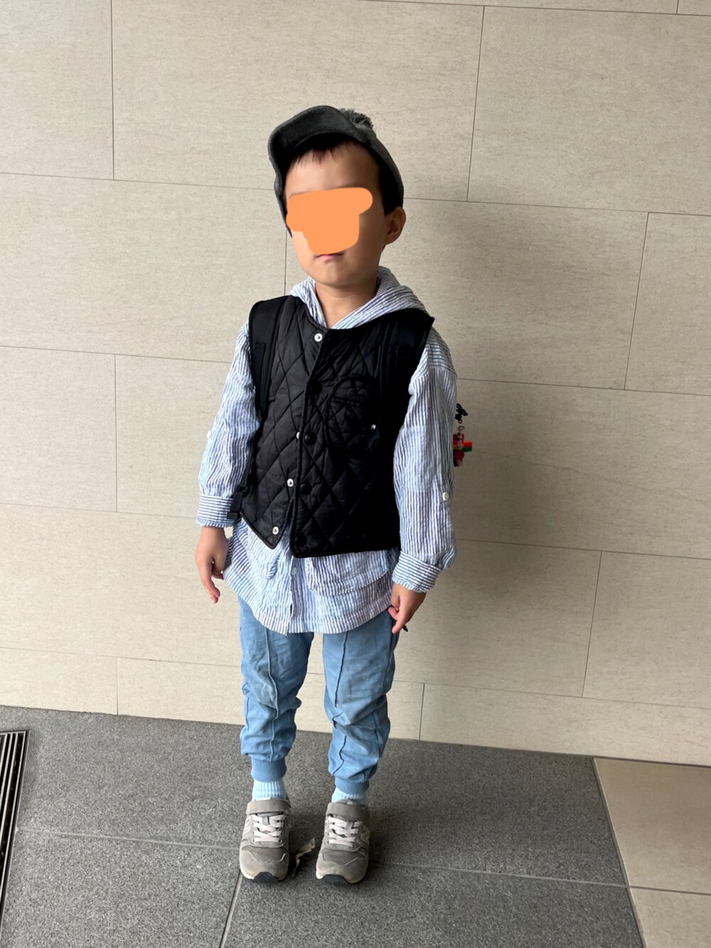 ブラック系のダウンベスト、ブルー系のパンツ、グレー系のスニーカーを着用したキッズの秋コーディネートの2枚目の写真