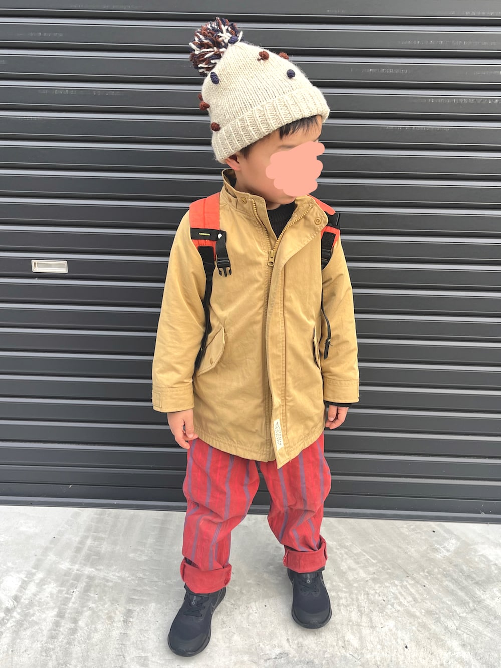 ベージュ系のモッズコート、レッド系のパンツ、ブラック系のスニーカーを着用したキッズの冬コーディネートの2枚目の写真