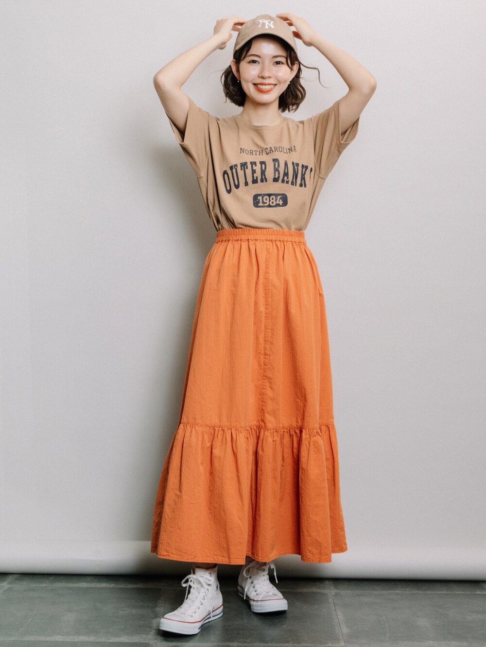 ブラウン系のTシャツ/カットソー、オレンジ系のスカート、ホワイト系のスニーカーを着用したレディースの春コーディネートの2枚目の写真