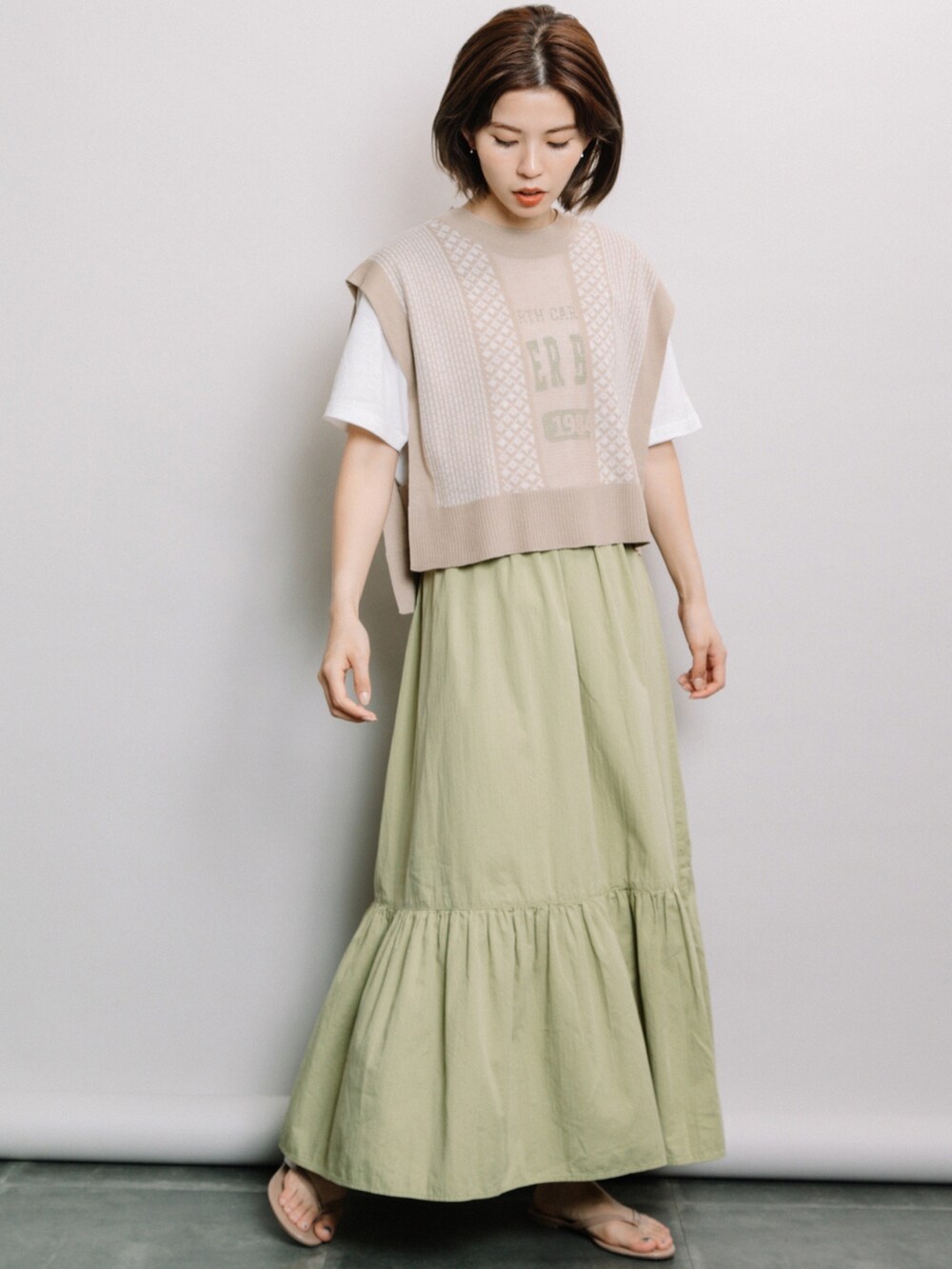 ベージュ系のベスト、グリーン系のスカート、ホワイト系のTシャツ/カットソーを着用したレディースの春コーディネートの2枚目の写真