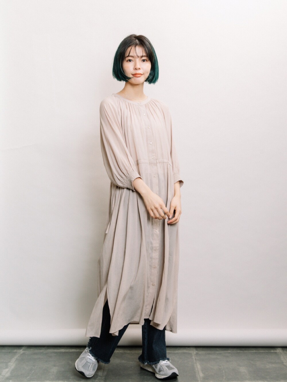 ベージュ系のワンピース、ブルー系のデニムパンツ、グレー系のスニーカーを着用したレディースの春コーディネートの2枚目の写真