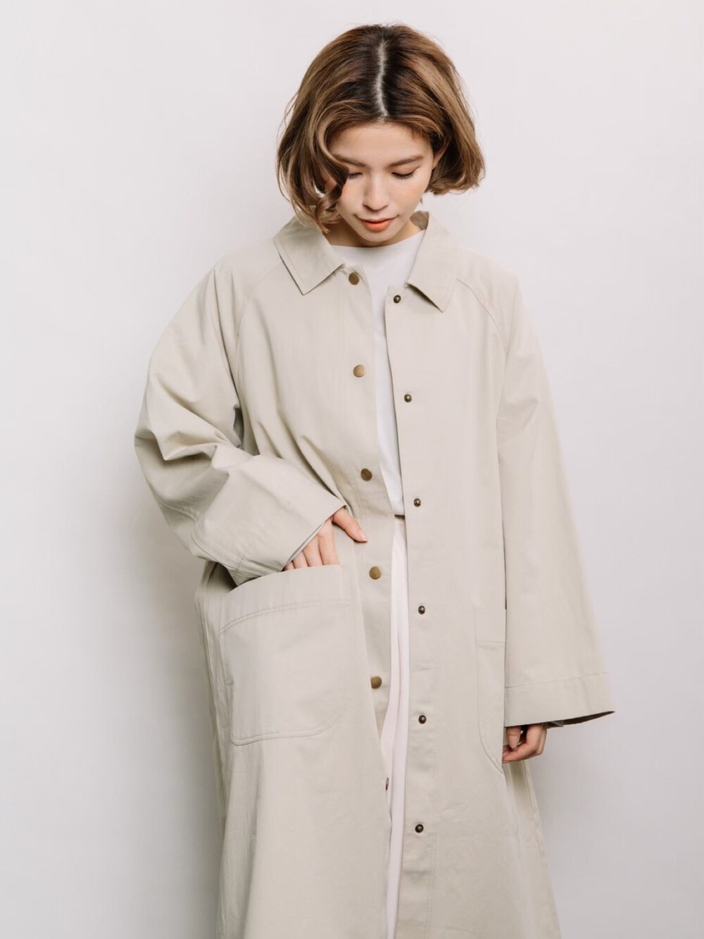 ベージュ系のステンカラーコート、ベージュ系のニット/セーター、ベージュ系のスカートを着用したレディースの春コーディネートの2枚目の写真