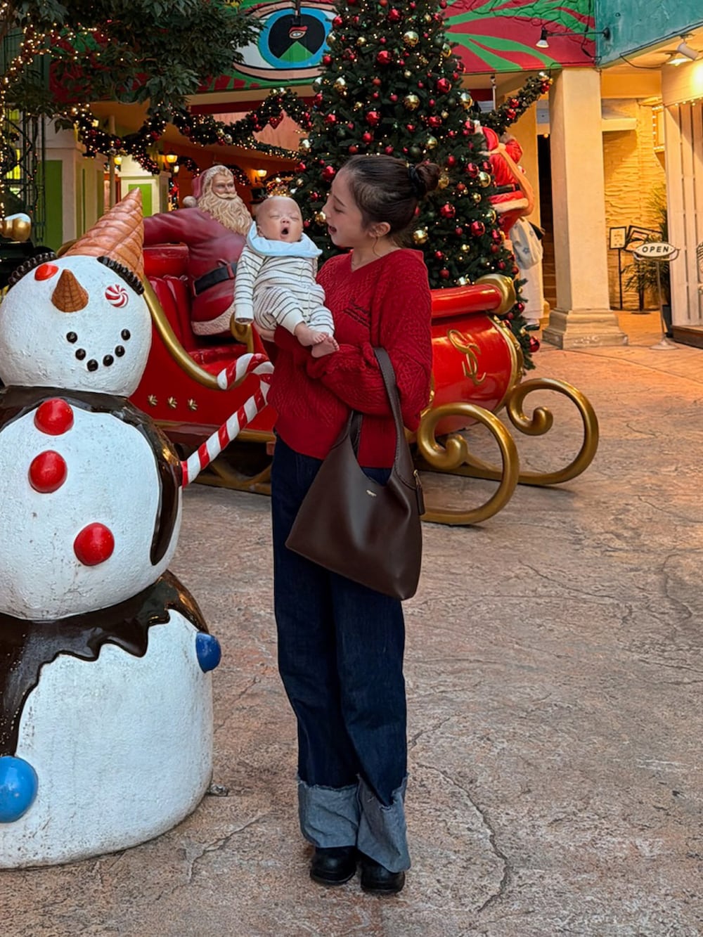 ブラウン系のショルダーバッグ、ブラック系のブーツ、レッド系のニット/セーターを着用したレディースの春コーディネートの2枚目の写真