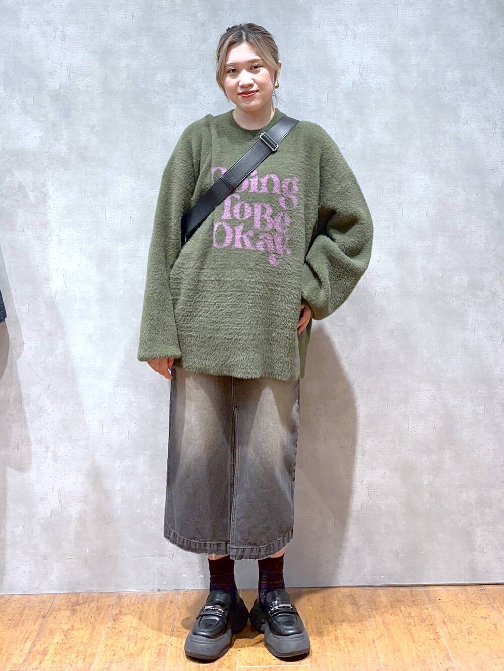 グリーン系のニット/セーター、ブラック系のショルダーバッグ、ブラック系のスカートを着用したレディースの秋コーディネートの2枚目の写真