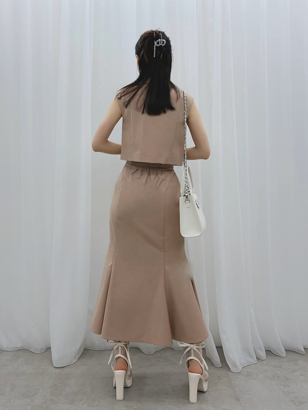 ベージュ系のスカート、ベージュ系のベスト、ホワイト系のサンダルを着用したレディースの夏コーディネートの3枚目の写真