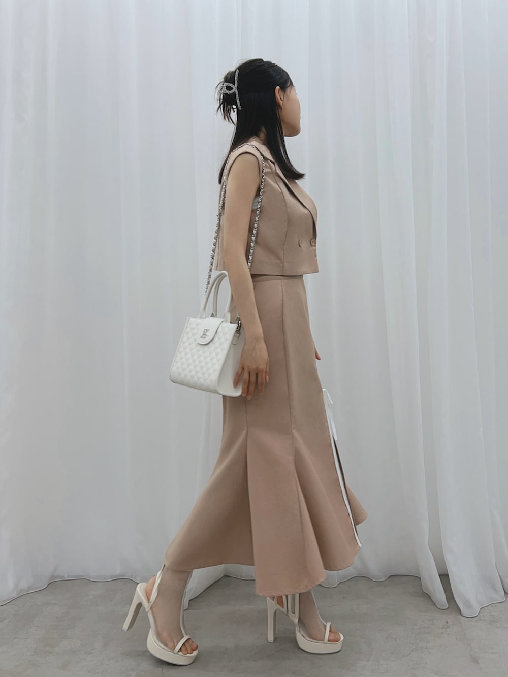 ベージュ系のスカート、ベージュ系のベスト、ホワイト系のサンダルを着用したレディースの夏コーディネートの2枚目の写真