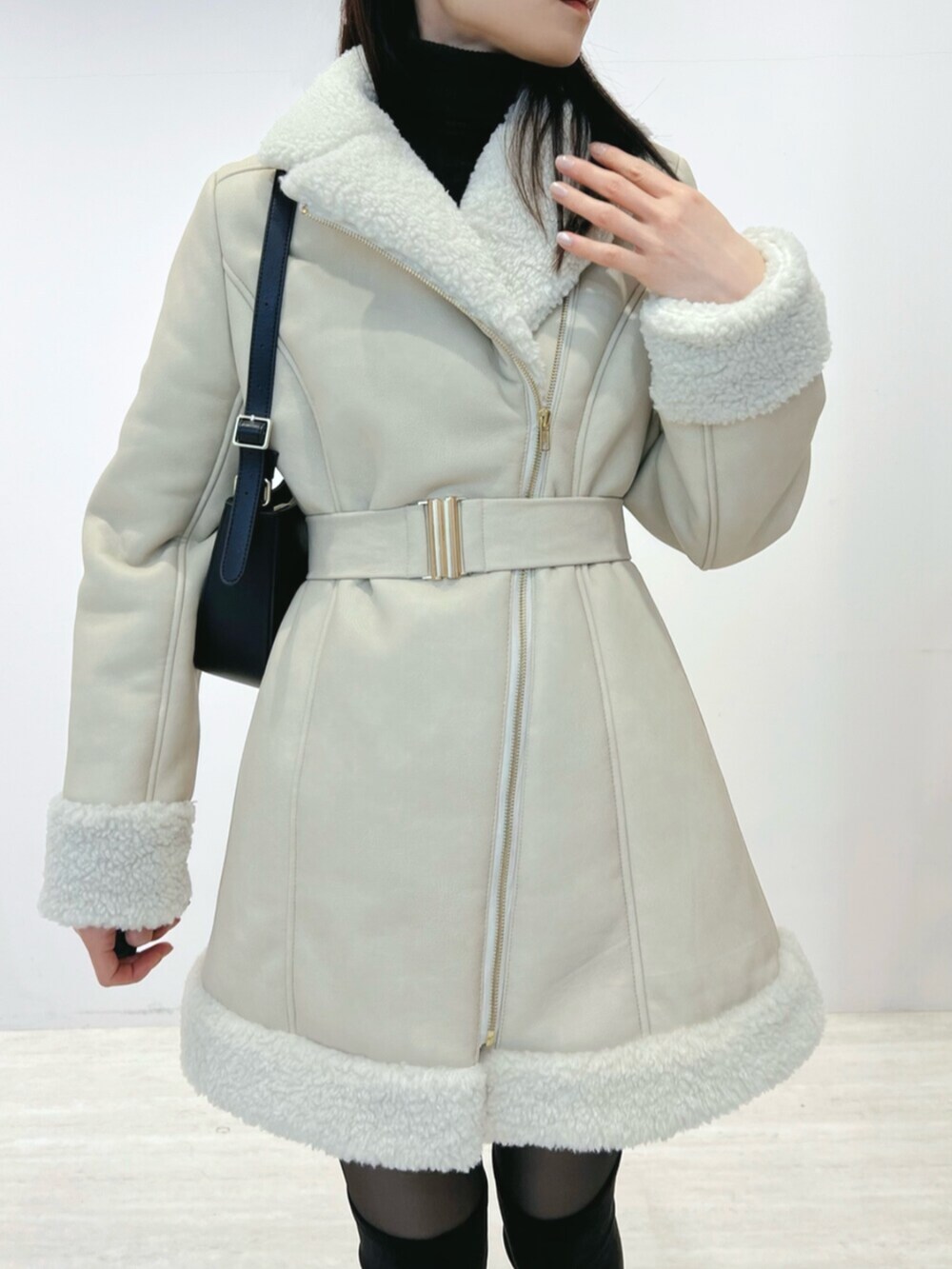 ブラック系のショルダーバッグ、ブラック系のブーツ、ベージュ系のムートンコートを着用したレディースの冬コーディネートの6枚目の写真