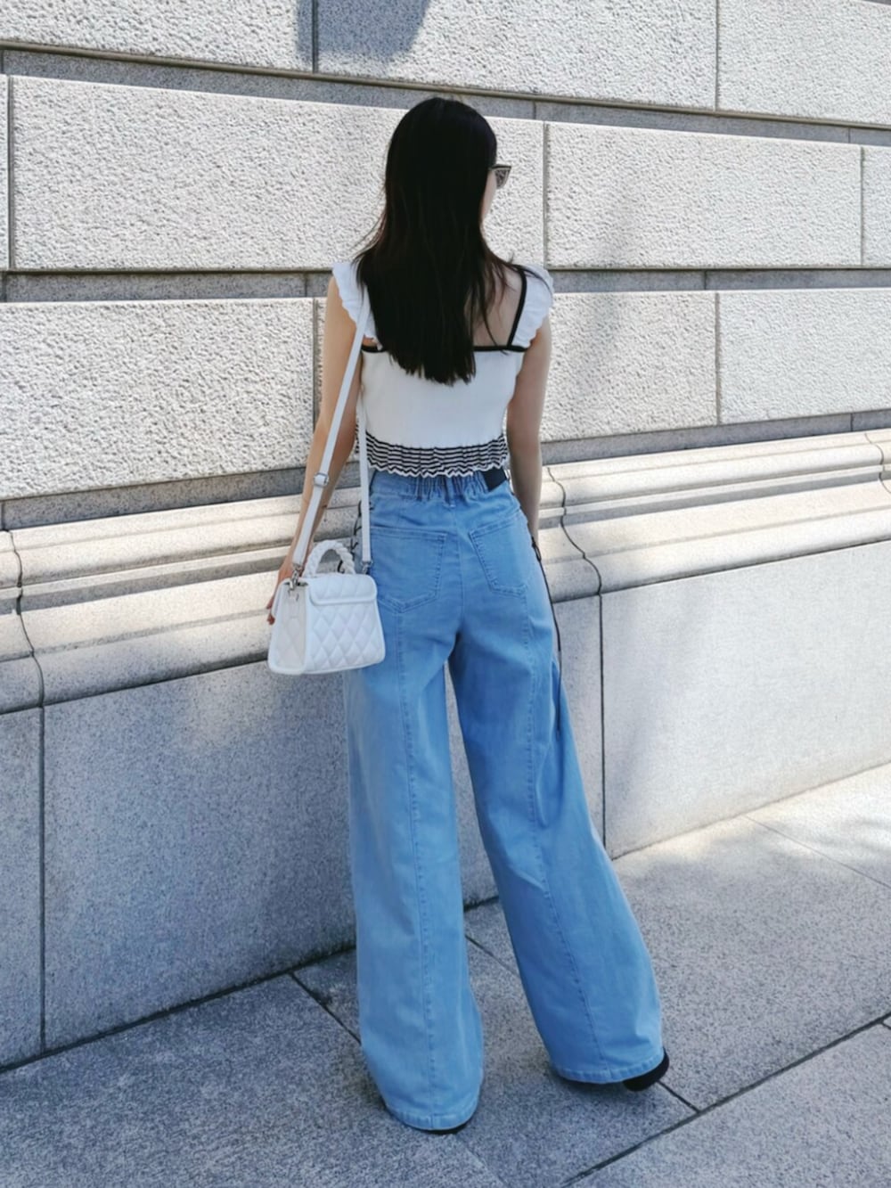 ブルー系のデニムパンツ、ホワイト系のキャミソール、ホワイト系のハンドバッグを着用したレディースの夏コーディネートの3枚目の写真