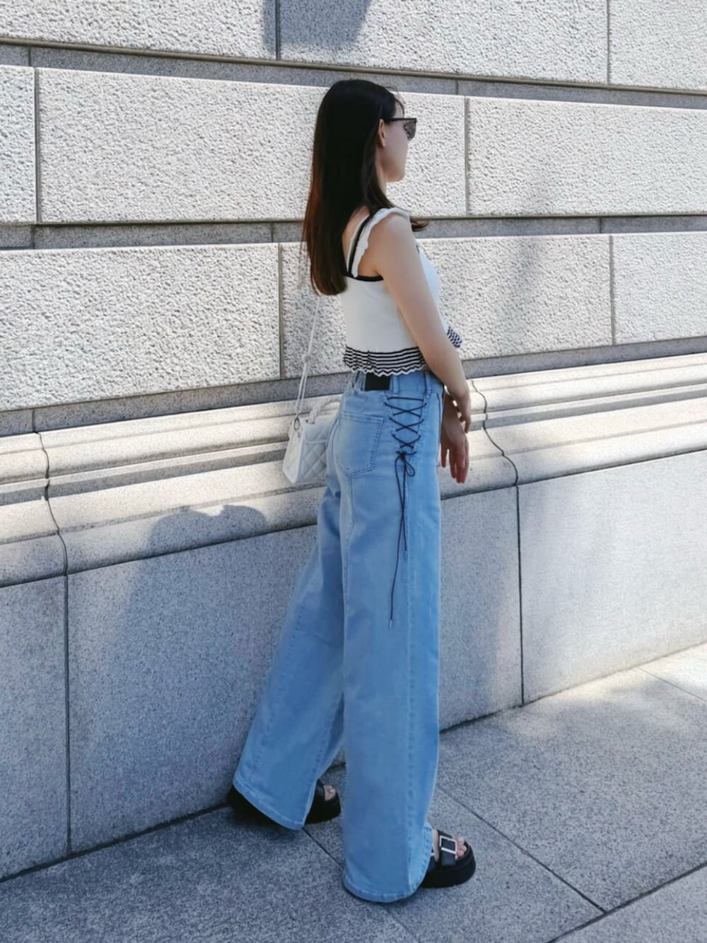 ブルー系のデニムパンツ、ホワイト系のキャミソール、ホワイト系のハンドバッグを着用したレディースの夏コーディネートの2枚目の写真