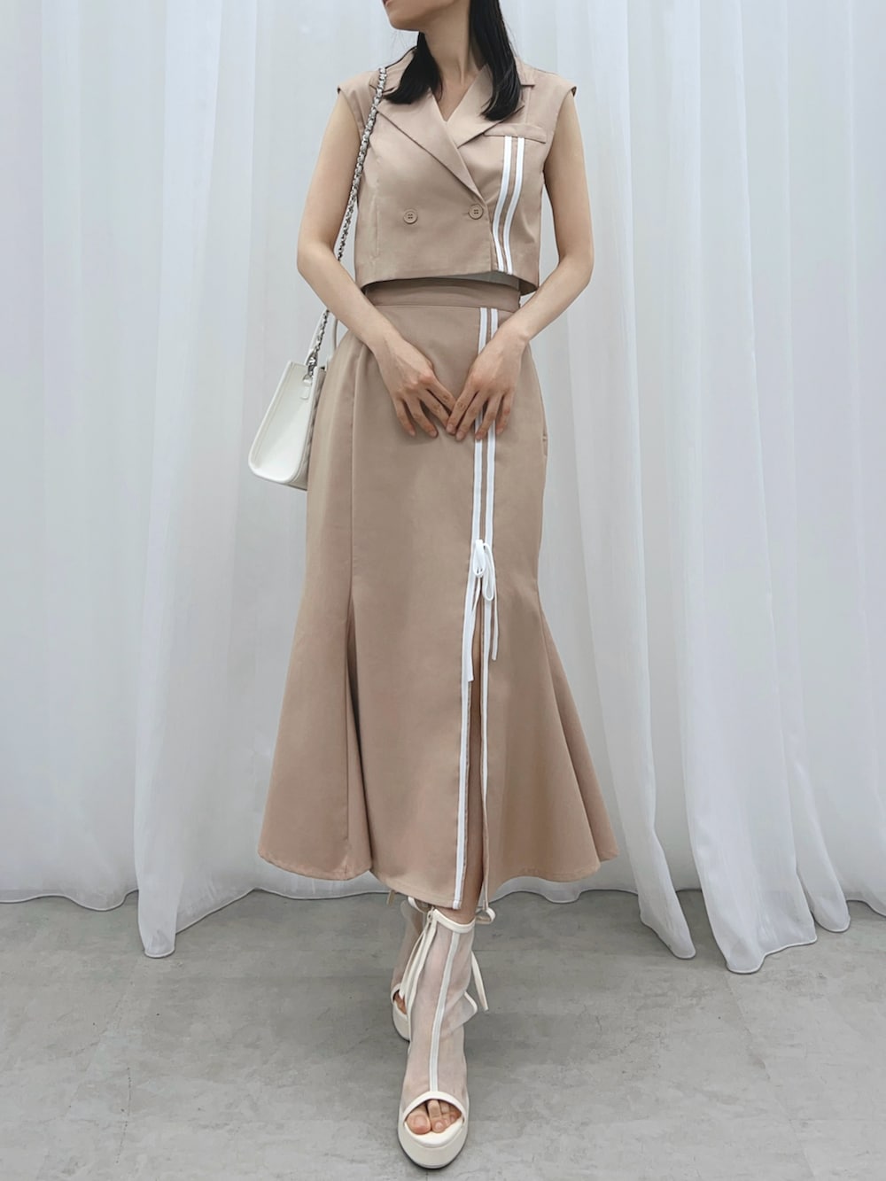 ベージュ系のスカート、ベージュ系のベスト、ホワイト系のサンダルを着用したレディースの夏コーディネートの4枚目の写真