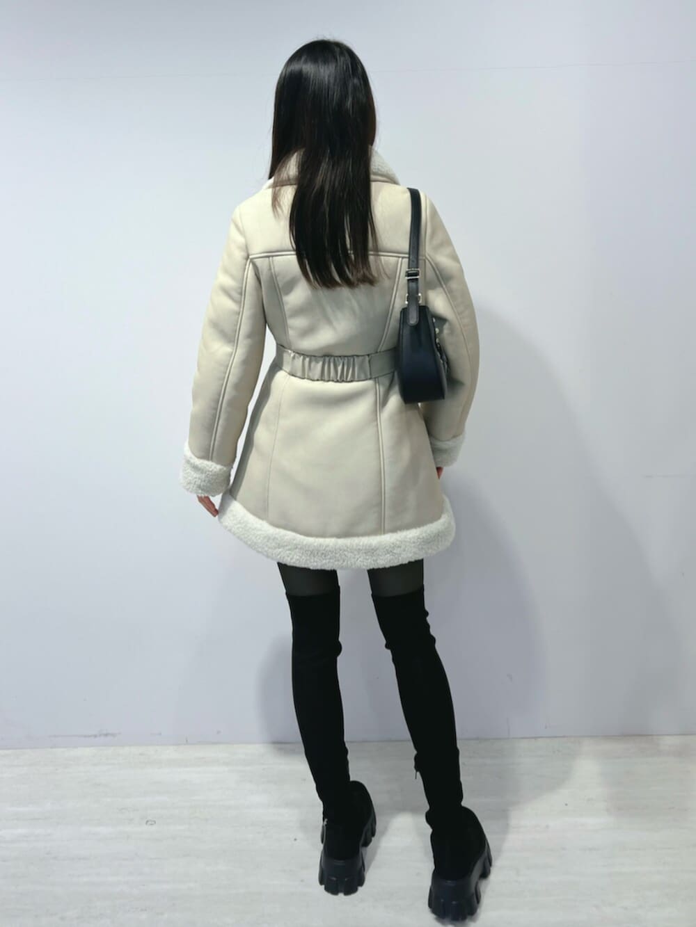 ブラック系のショルダーバッグ、ブラック系のブーツ、ベージュ系のムートンコートを着用したレディースの冬コーディネートの4枚目の写真