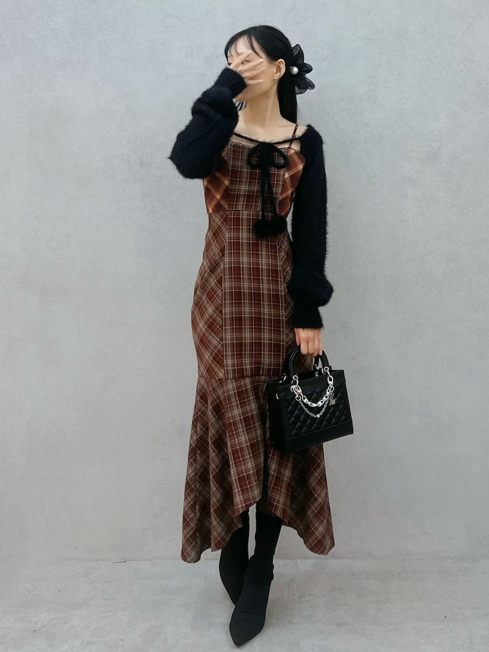 レッド系のワンピース、ブラック系のニット/セーター、ブラック系のブーツを着用したレディースの秋コーディネートの2枚目の写真