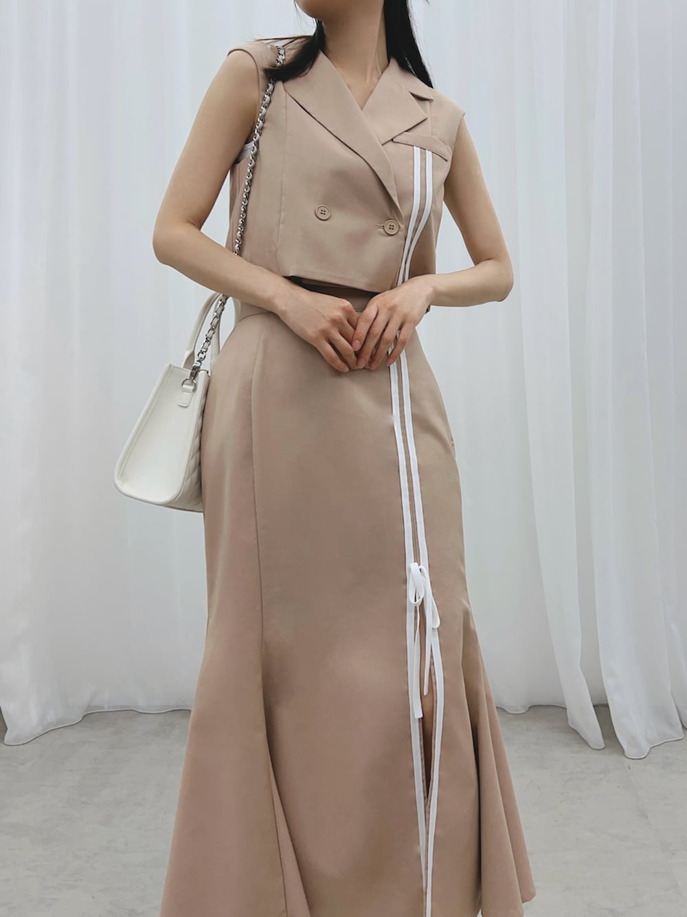 ベージュ系のスカート、ベージュ系のベスト、ホワイト系のサンダルを着用したレディースの夏コーディネートの5枚目の写真