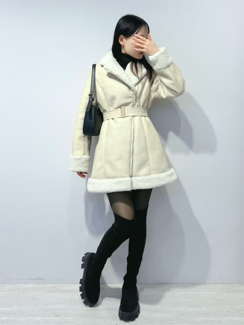 ブラック系のショルダーバッグ、ブラック系のブーツ、ベージュ系のムートンコートを着用したレディースの冬コーディネートの2枚目の写真