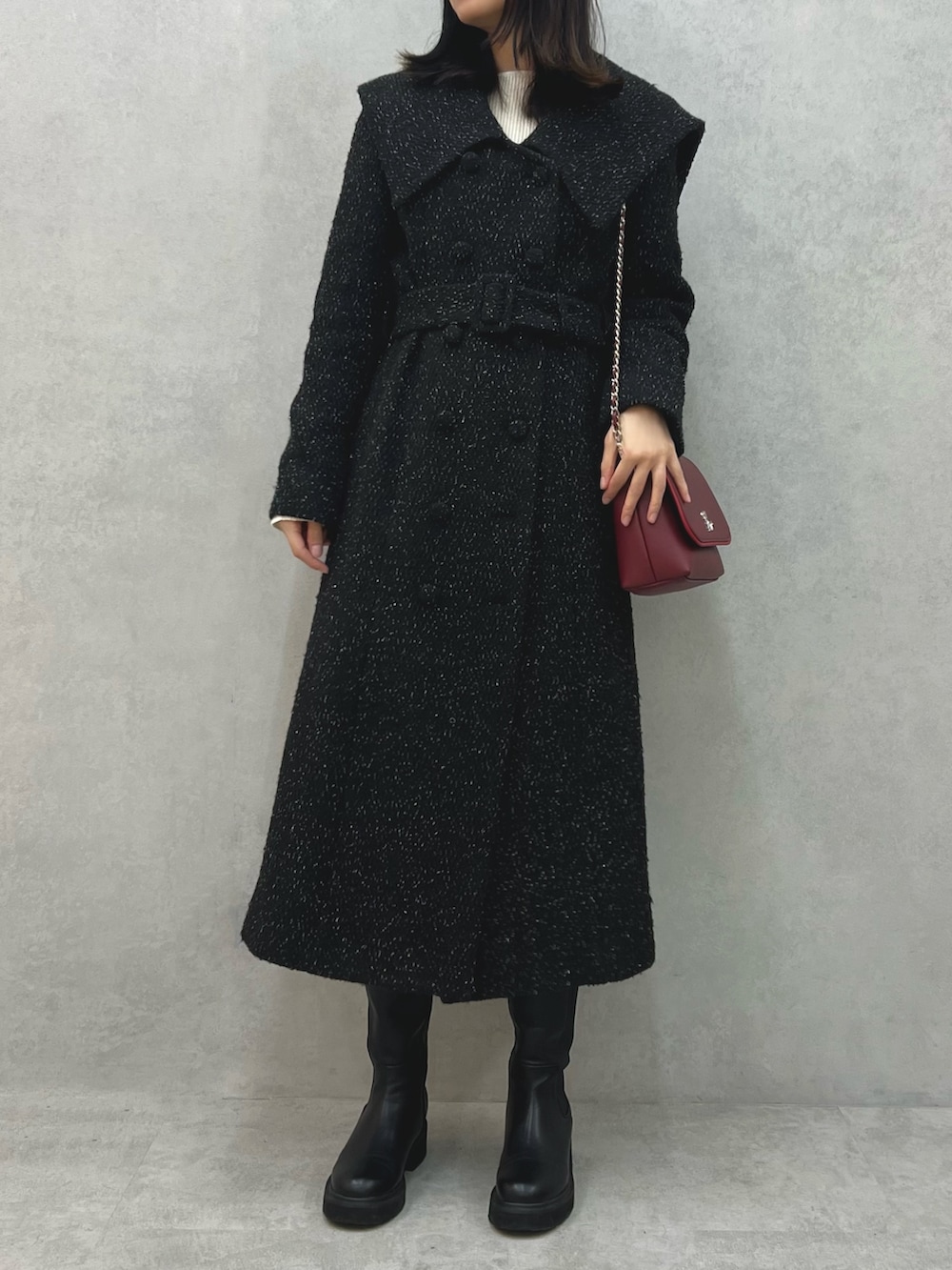 ブラック系のチェスターコート、レッド系のショルダーバッグ、ホワイト系のニット/セーターを着用したレディースの冬コーディネートの2枚目の写真