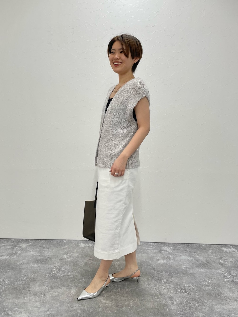 ベージュ系のベスト、ホワイト系のスカート、ブラック系のトートバッグを着用したレディースの春コーディネートの4枚目の写真